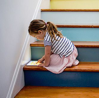 Petite fille joue avec une tablette sur les escaliers.